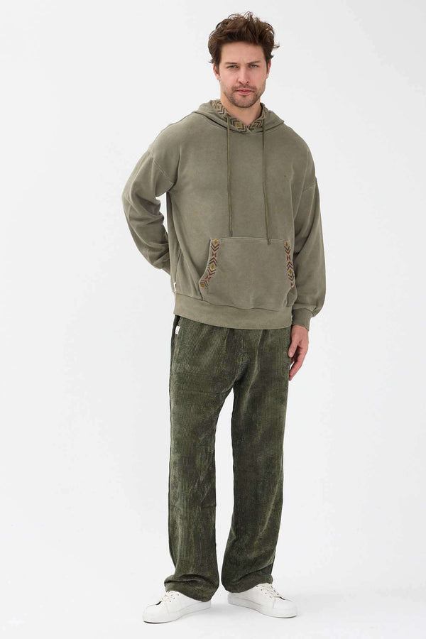Sage Kapşonlu Nakışlı Sweatshirt üzerinde bir adam, yeşil pantolonla birlikte, rahat bir görünüm sergiliyor.